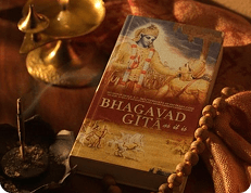 Bhagavad Gita book beside a brass lamp and prayer beads