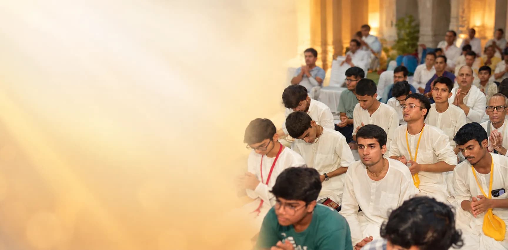 Young devotees in white seated together with folded hands