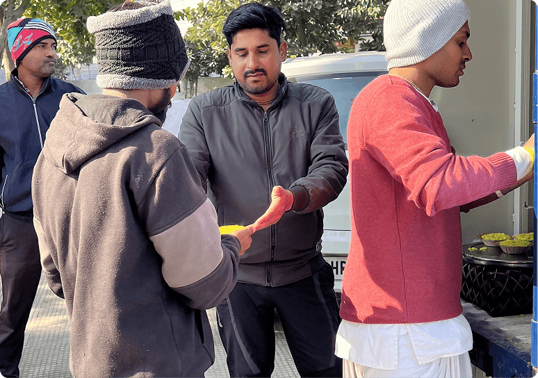 A volunteer placing warm prasadam into waiting hands