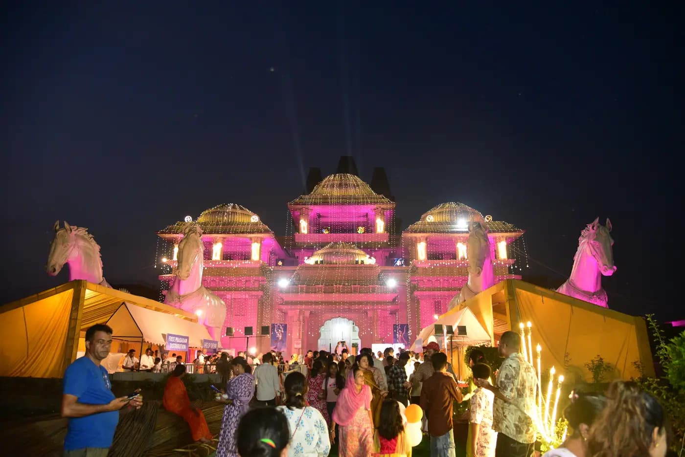 The temple lit up at night, with devotees gathered on the grounds
