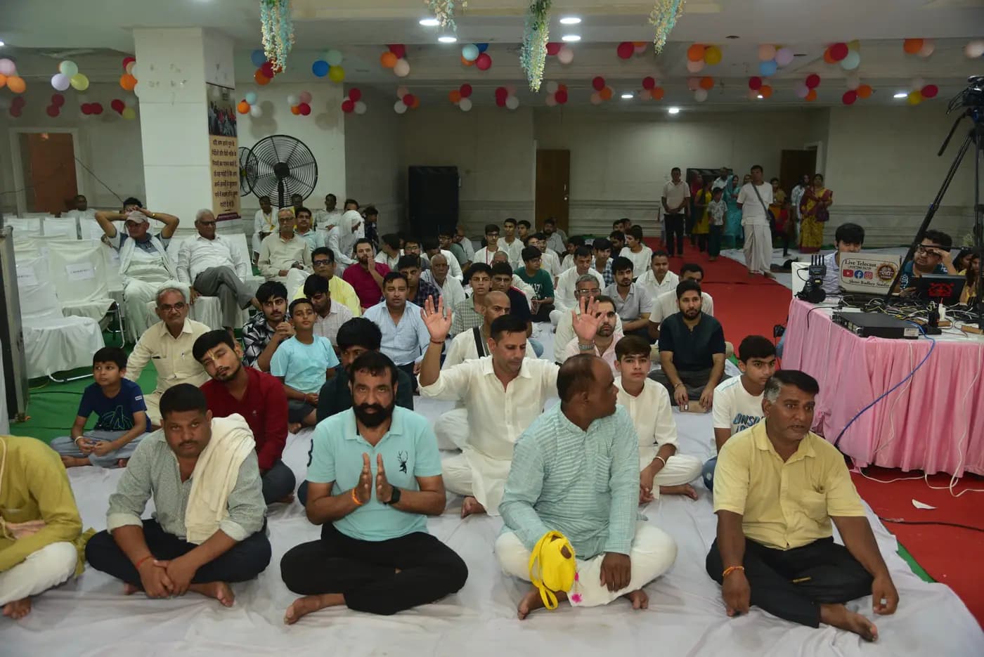 Devotees seated together in the temple hall with hands raised during kirtan