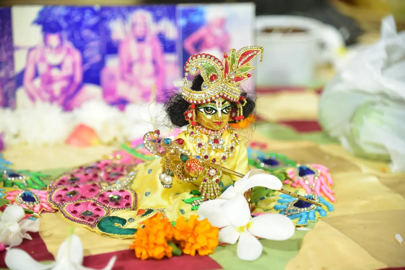 Laddu Gopal dressed in yellow silk with a jewelled crown and flute, surrounded by flowers