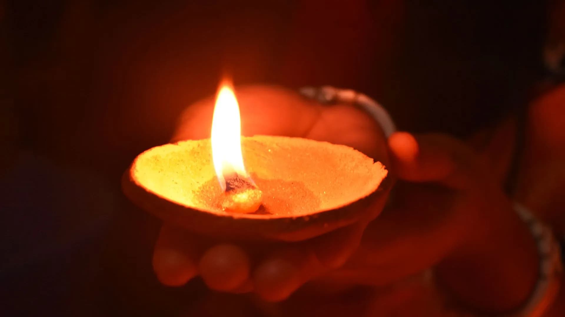 A lit ghee lamp held in a devotee’s cupped hands
