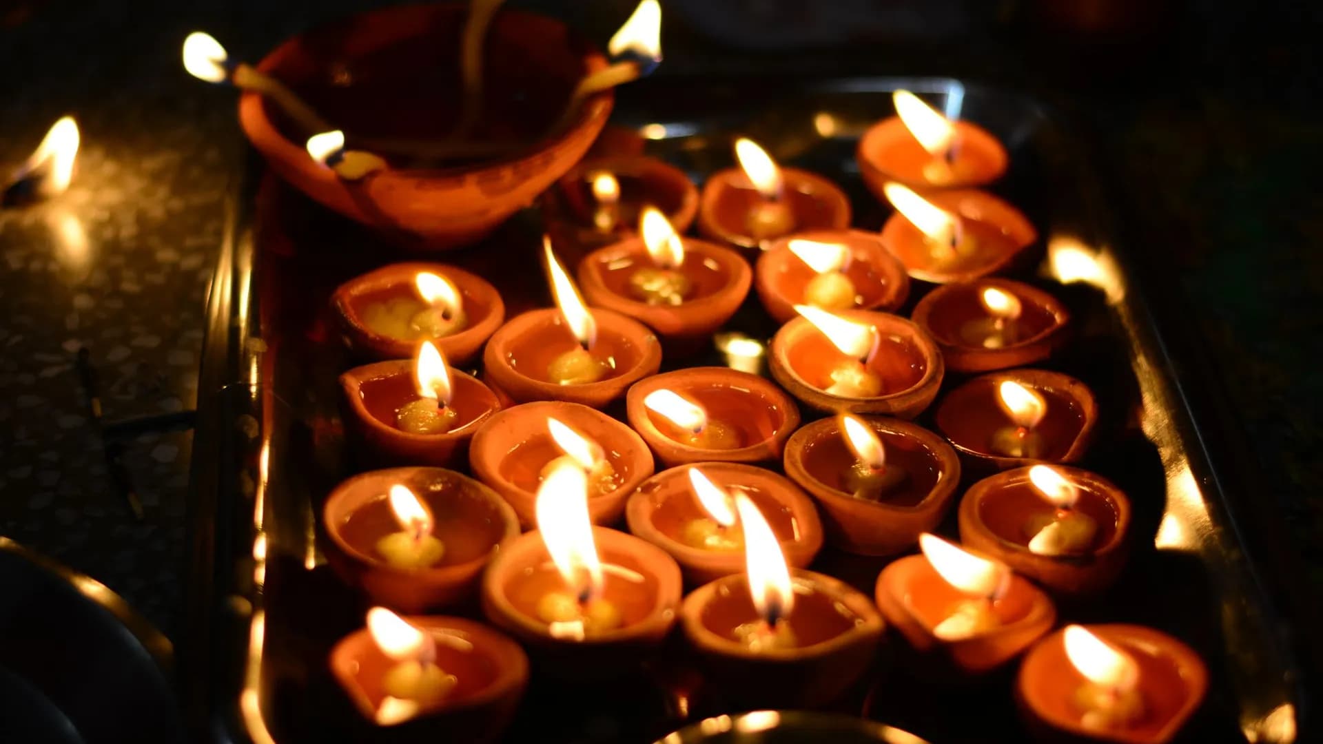 Rows of lit clay lamps on a tray for the Kartik evening offering