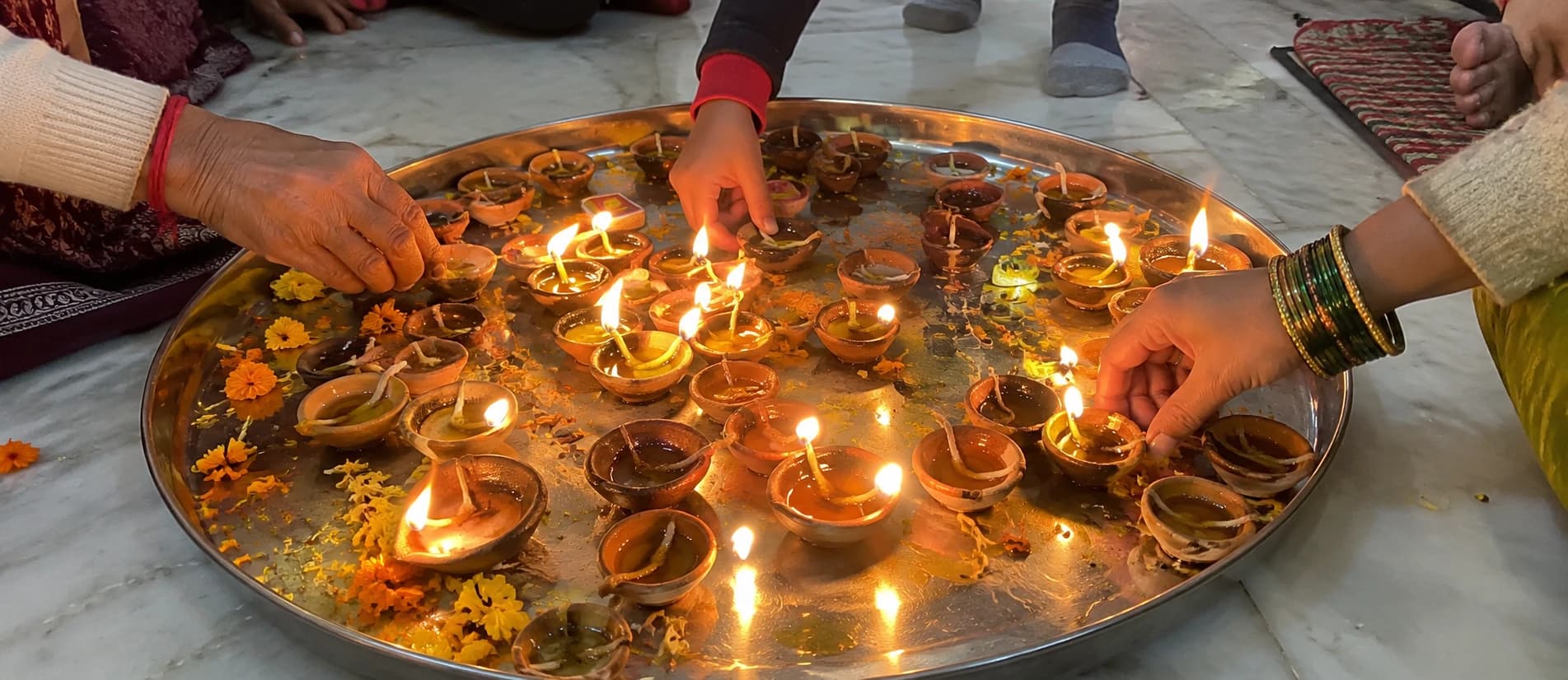 Devotees’ hands placing lit lamps on a large tray decorated with marigolds